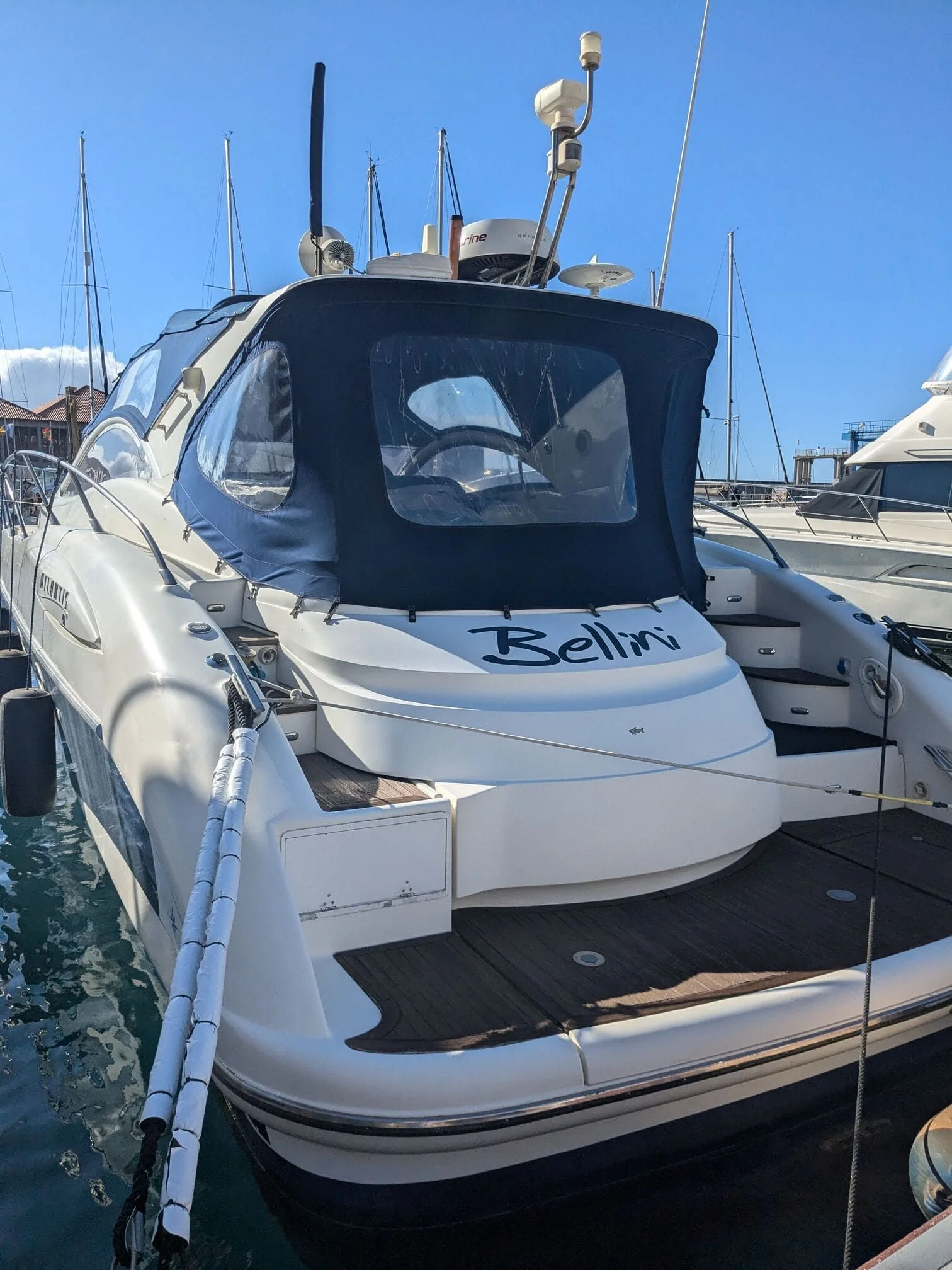 White cabin cruiser moored at St. Petersburg marina with canvas canopy and navigation equipment visible.