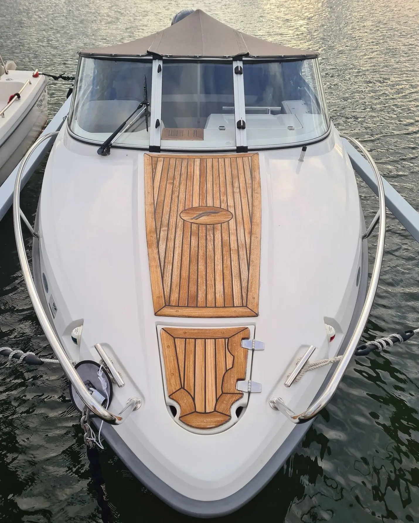 Overhead view of white recreational fishing boat with teak deck and canvas canopy on water.