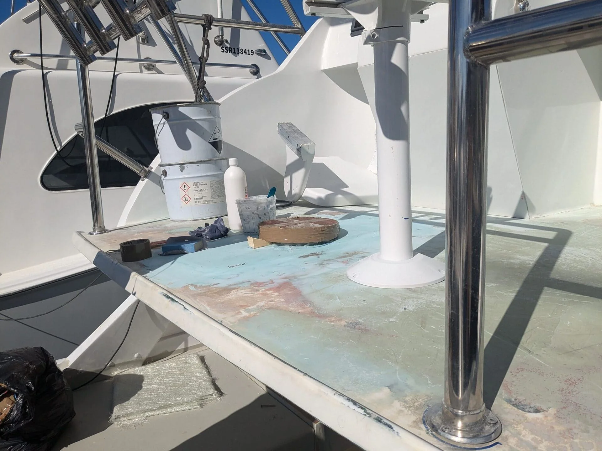 Boat deck with repair materials and chemical containers during maintenance work in bright sunlight.