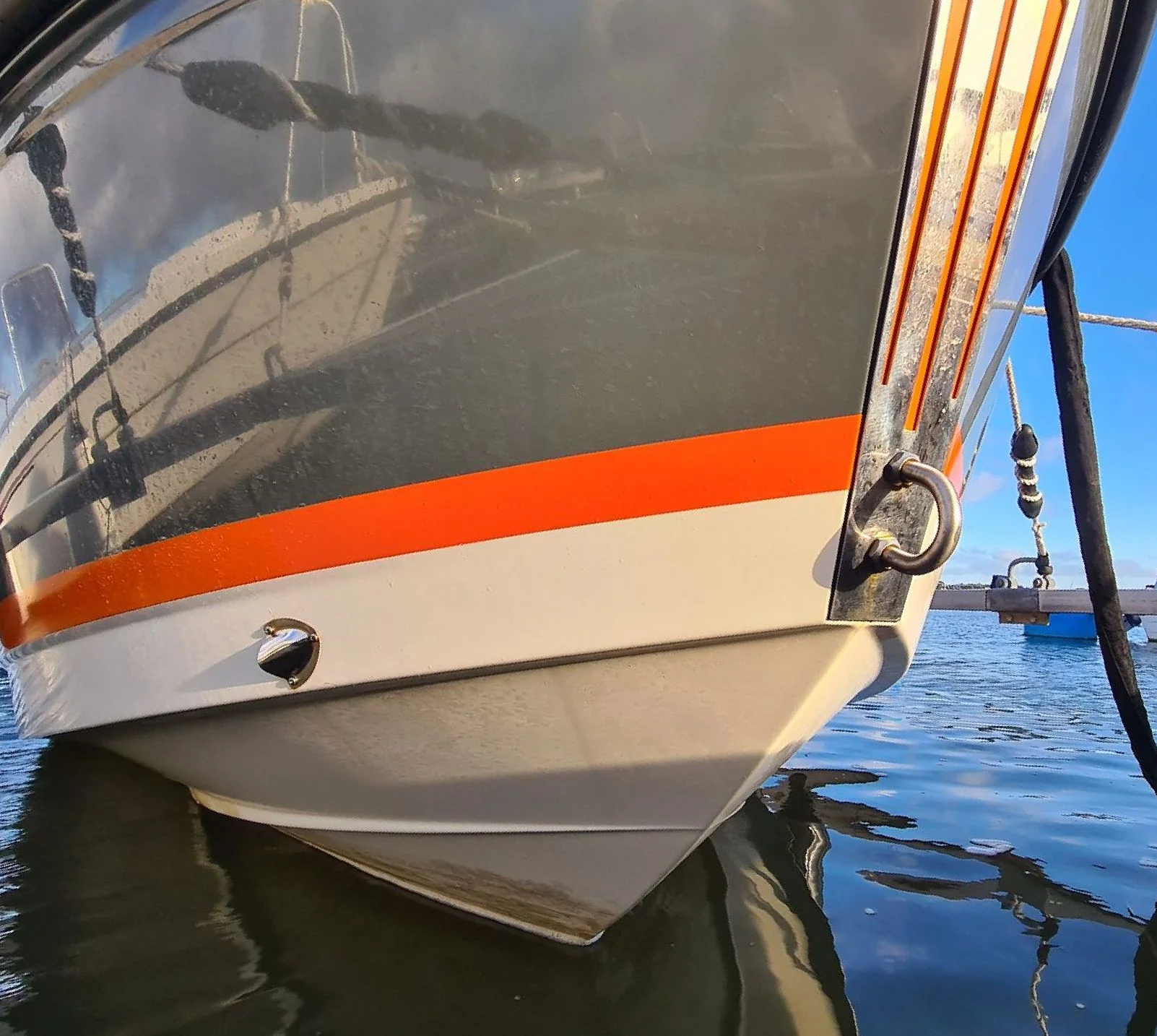 Boat hull with orange stripe moored in calm Florida waters, showing weathered gelcoat and hardware.