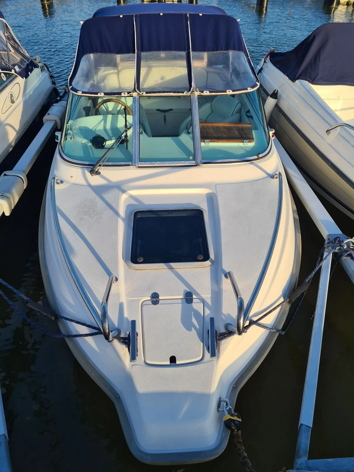 White recreational fishing boat moored at St. Petersburg dock with canvas canopy and steering wheel visible.