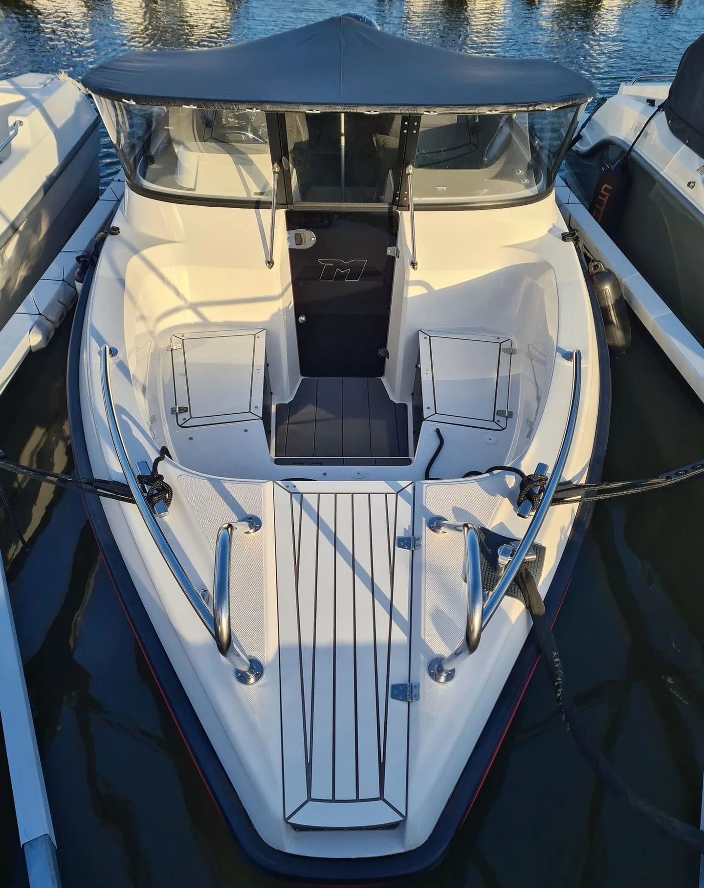 White recreational fishing boat moored in calm water, overhead view showing cabin, seating, and open deck layout.