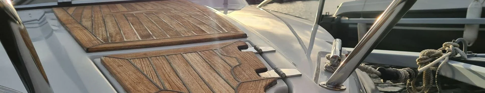 Wooden boat deck with teak planking and stainless steel hardware in bright sunlight.