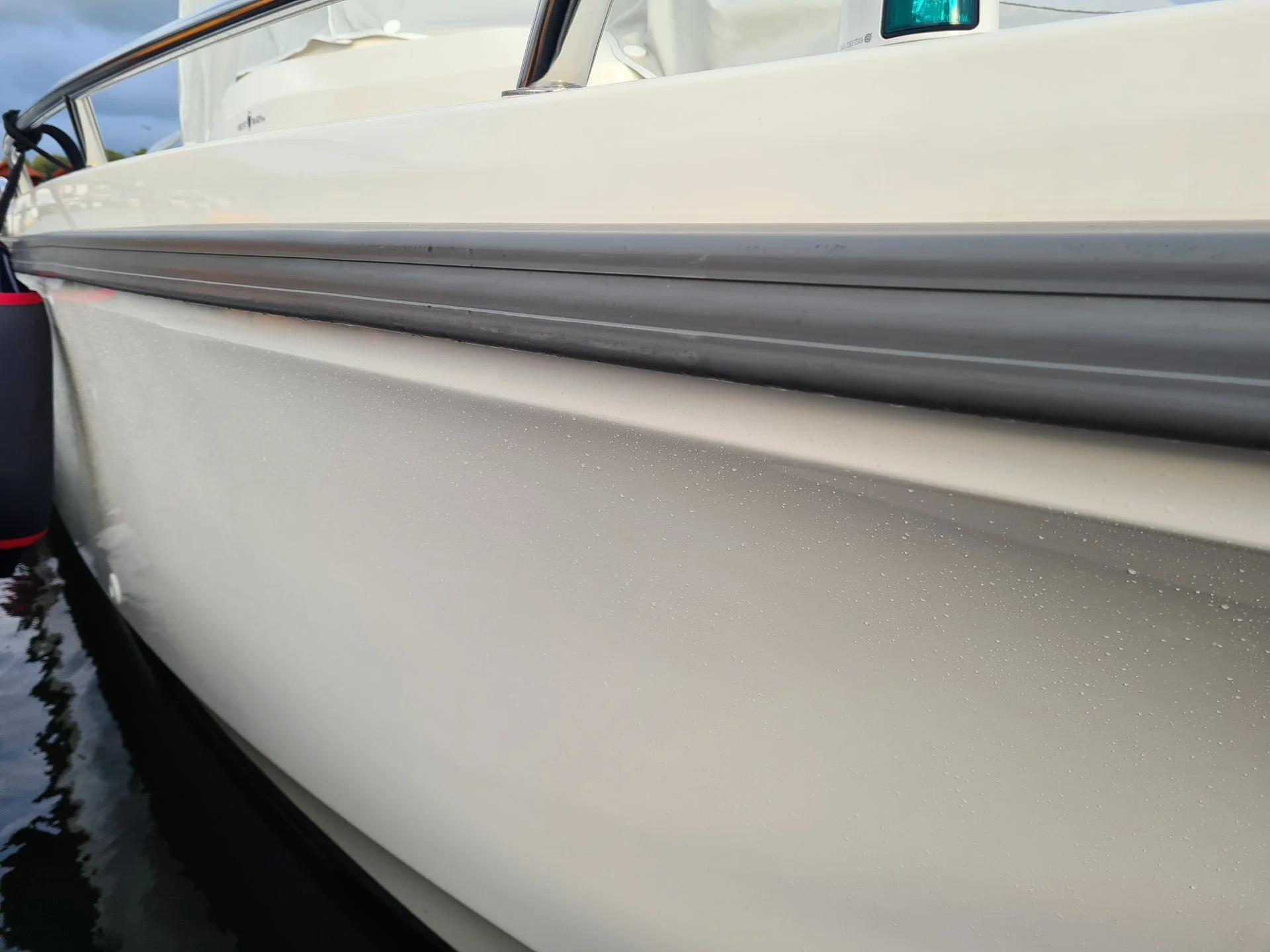 Boat hull detail showing white gelcoat surface with water droplets and gray rubbing strake.