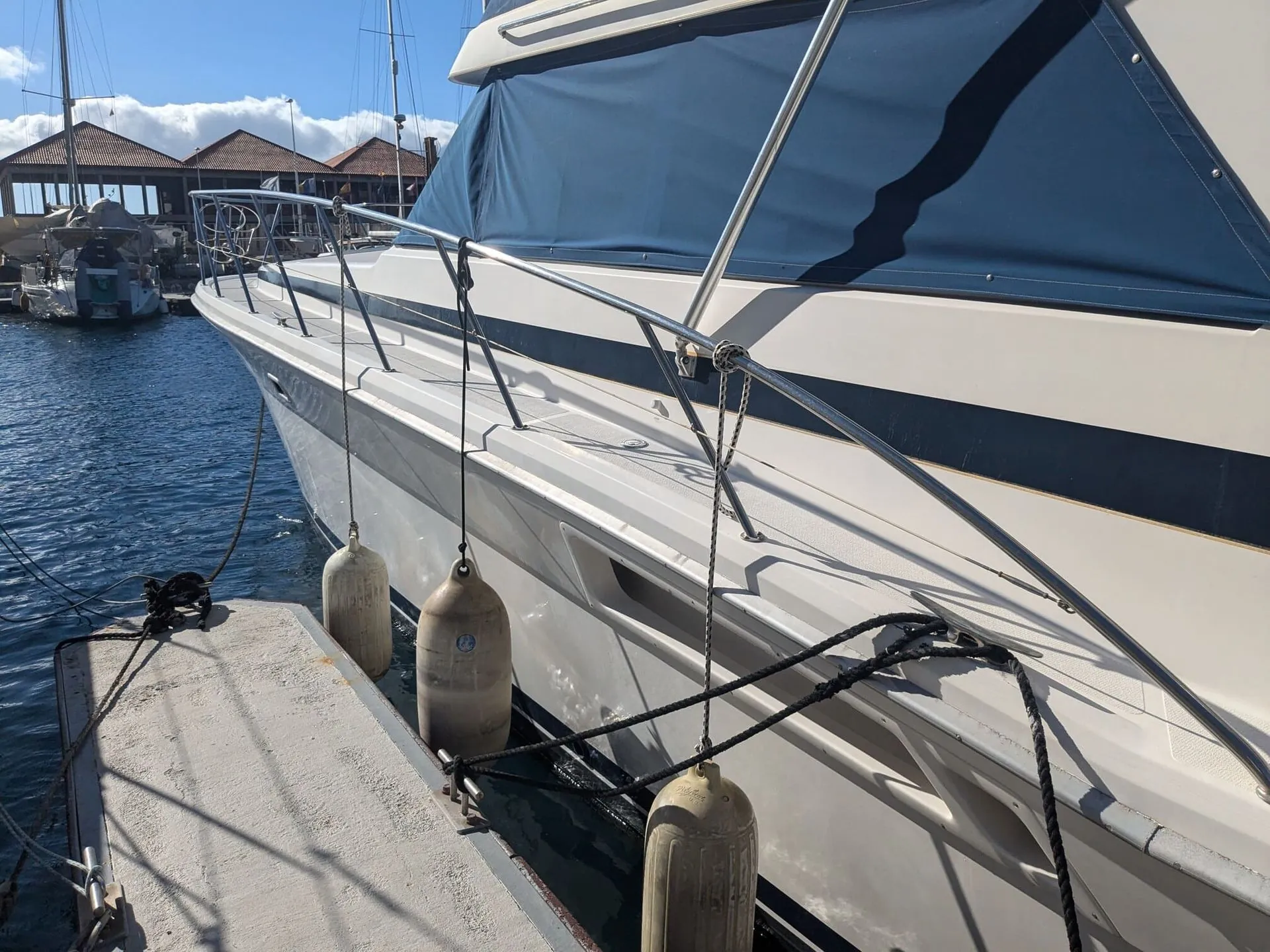 Sailboat moored at St. Petersburg dock with canvas canopy and fender lines visible.