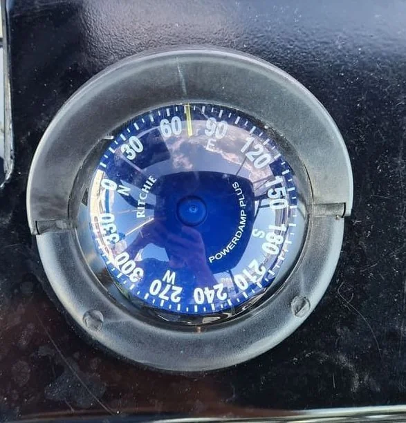 Marine compass gauge mounted on dark boat dashboard showing directional readings.