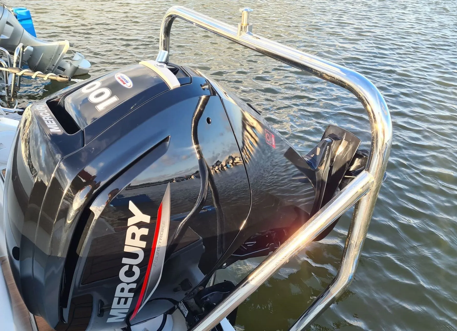 Outboard motor mounted on boat transom at waterside, showing engine detail and chrome railings.